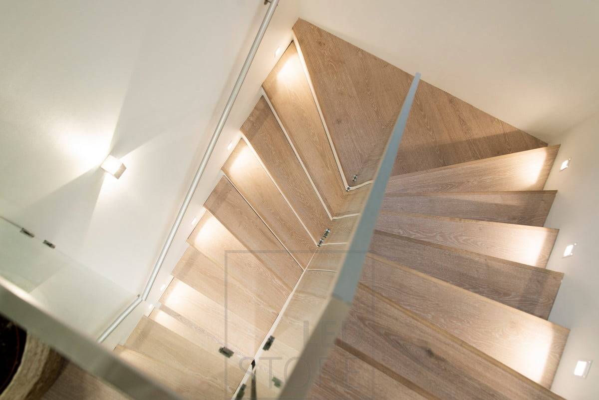 Iluminación de escalera, con una lámpara de peldaño en cada segundo peldaño y luminarias bidireccionales en la pared.